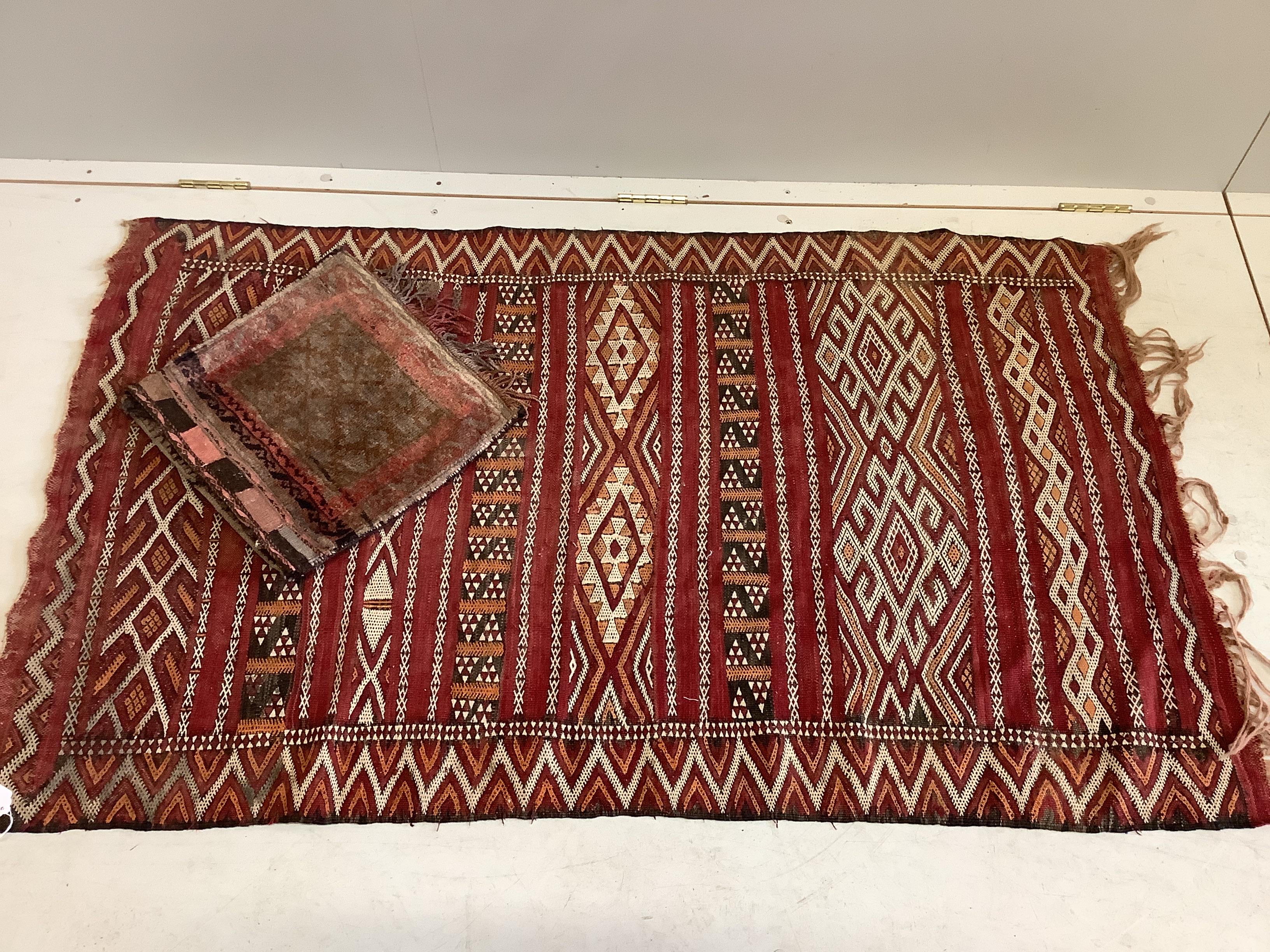 A Moroccan red ground geometric rug together with a saddle bag, larger 150 x 90cm